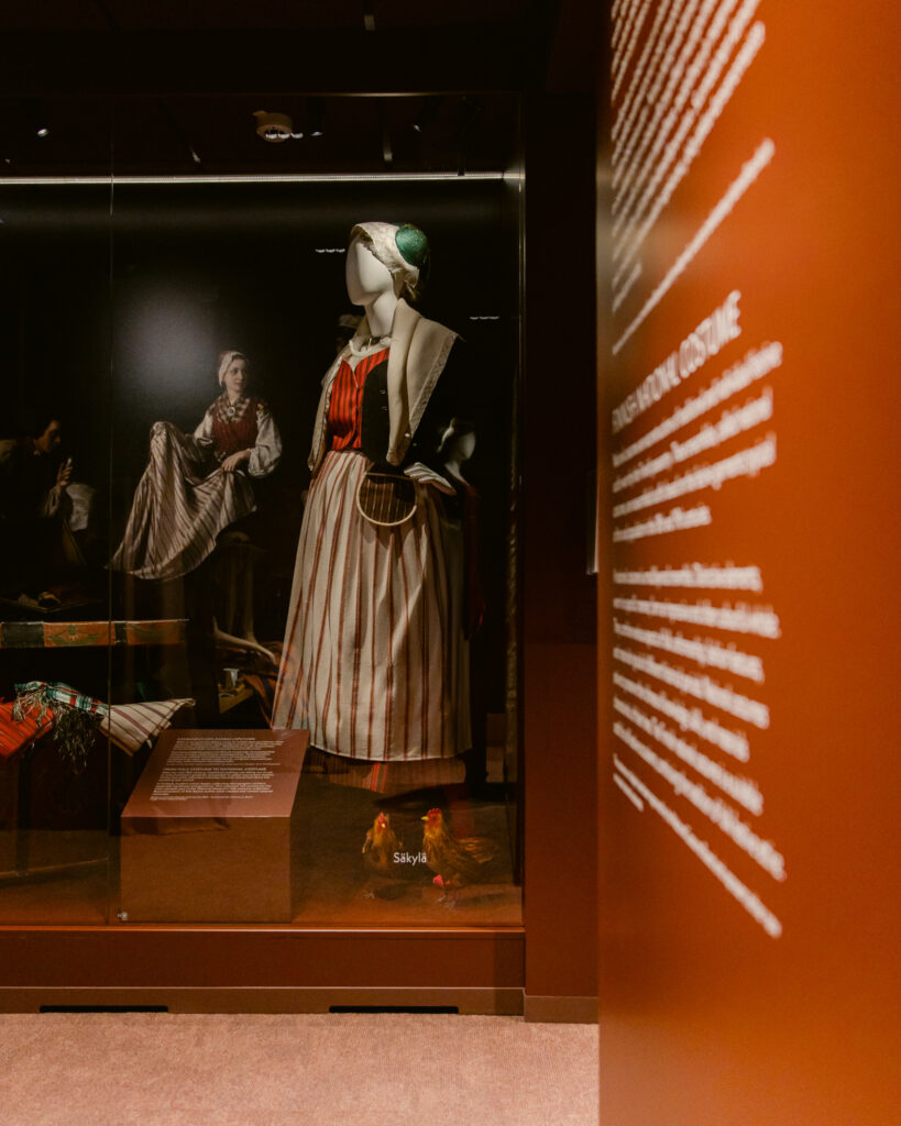 Kansallispuvut osana museaalista näyttelyarkkitehtuuria Esinekeskeinen näyttelyarkkitehtuuri museossa, jossa kansallispuvut on esitelty ilmavasti ja arvokkaasti.