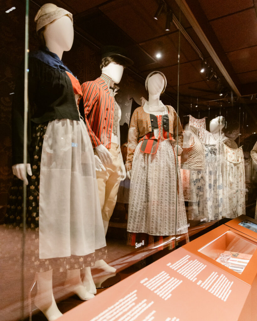 Neutraali tausta kansallispukujen näyttelyssä Museaalinen näyttelyarkkitehtuuri museossa, jossa neutraali tausta korostaa kansallispukujen värejä ja yksityiskohtia.