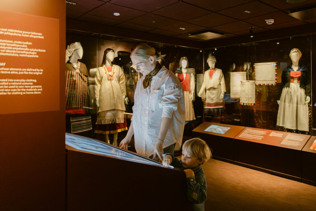 Näyttelyarkkitehtuuri museossa, jossa Suomen kansallispukukeskuksen pysyvä näyttely avautuu rauhallisena ja arvokkaana kokonaisuutena.