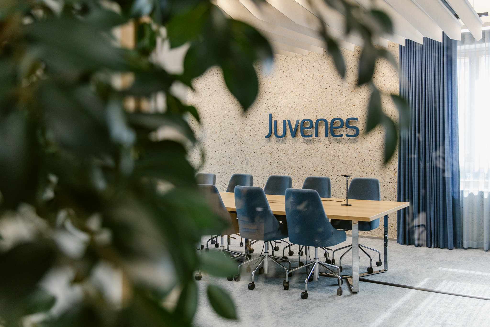 Kestävä toimistosuunnittelu, neuvottelutila Juvenes Juveneksen neuvottelutila, jonka seinällä logo kierrätysmateriaalipinnalla ja siniset akustoivat verhot